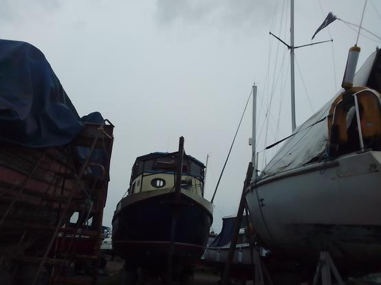 A boatyard view, centre of shot from a reclining position, a steel lifeboat conversion into a now seriously neglected river boat