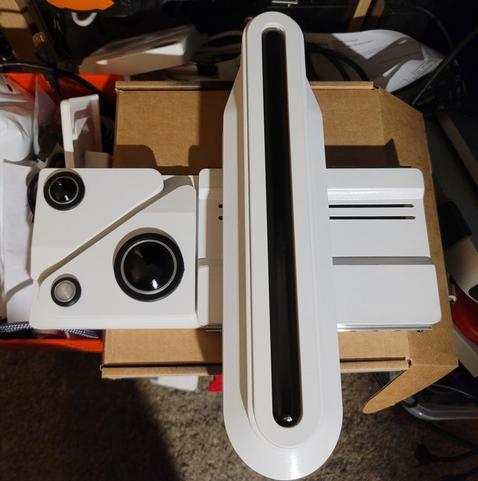 A 3D model replica of the baseline scanner from blade runner 2049. It is a gloss white device with a horizontal based and a vertical, sliding ngscanner with a black shiny bar in the center. There are three other lenses on the left hand side.