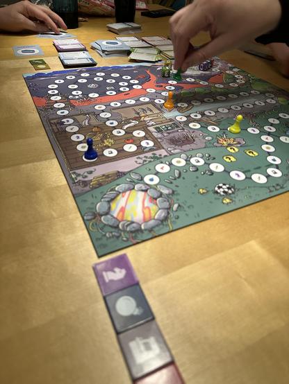 Spielbrett mit Bildern im Videogame-Comic-Style. Eine Hand setzt eine Figur weiter.