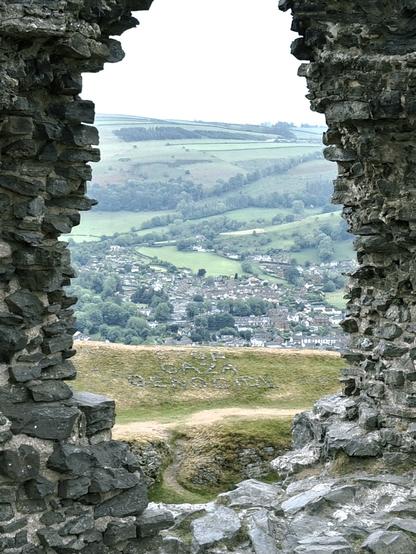 View through stony ruins of arched castle window, showing spot and proximity of the message "Stop Gaza Genocide" in rocks on the rampart beyond
