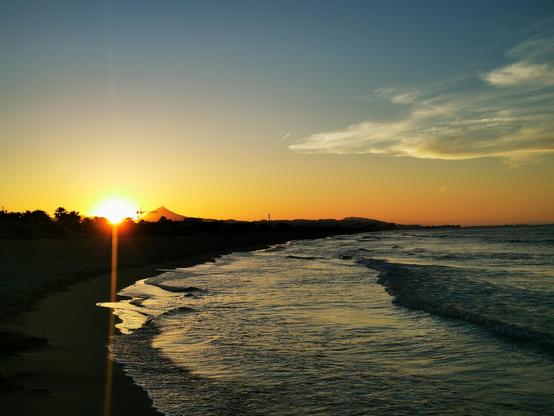 Sonnenuntergang am Strand. Man sieht das Meer, und die Sonne, die hinter den Dünen untergeht