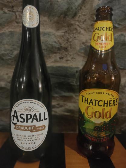Two bottles of cider.  One is Aspall Draught Cider , the other Thatches Gold