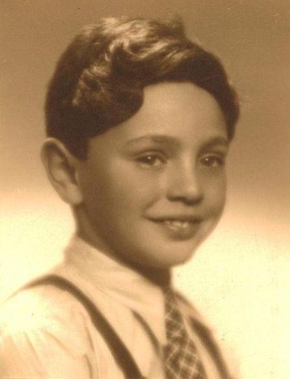 Vintage sepia portrait of a smiling child with neatly combed hair, wearing a shirt, tie, and suspenders.