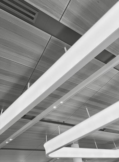 Black and white photograph looking up at the ceiling in an airport. Curved bars of lighting snake over wooden panels.