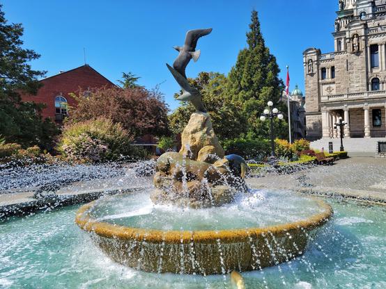 This is mostly an image of the fountain at the back of the BC Legislature. The fountain is in two tiers, with an elevated portion in the middle. In the middle of the second tier is a sculpture of some rocks being shared by a family of otters with two seabirds flying overhead.

Someone has added dish soap to the water (unfortunately not uncommon), hence the suds.