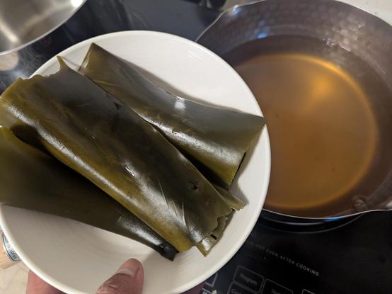 A bowl with rehydrated kelp and in the background a pot with light amber dashi