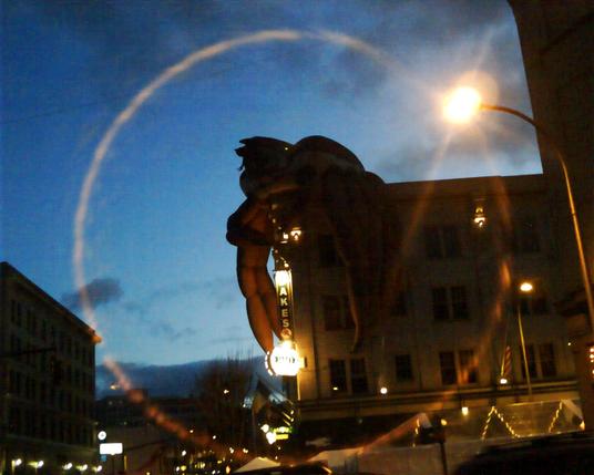 Twilight shot/ of a giant inflatable crab on top of a downtown Portland, Oregon building. There is a circular lens flare surrounding the whole thing.