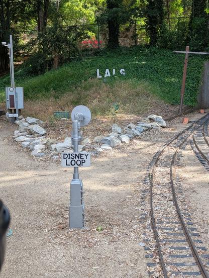 The LA Live Steamers logo on a hill next to a sign that says "Disney Loop" (which goes around Walt's Barn)