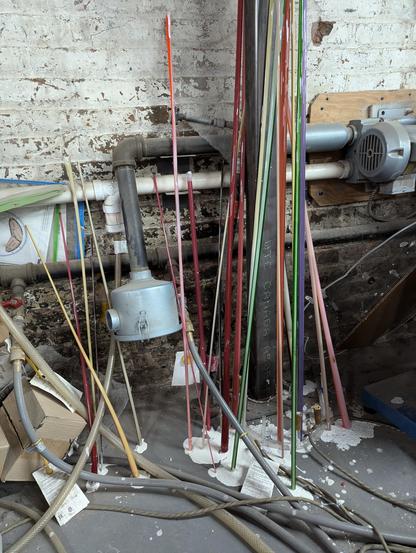 A bunch of glass tubes in various colors. lengths and sizes leaning up against a white brick wall with white paint leaking from the bottom of all the tubes.