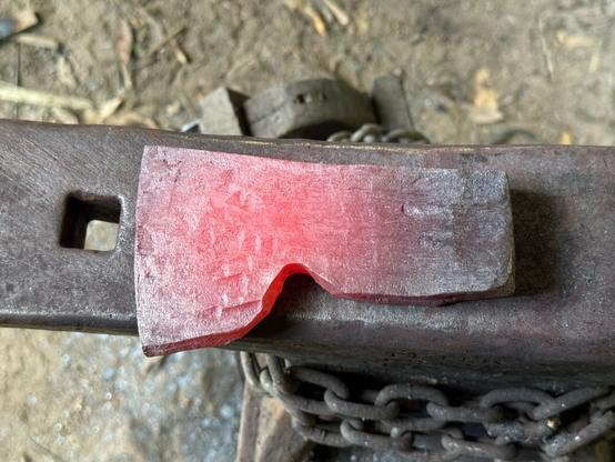 The beginnings of a bearded axe head sitting on the anvil. The blade end is glowing a nice maraschino cherry red, while the pole is barely glowing.