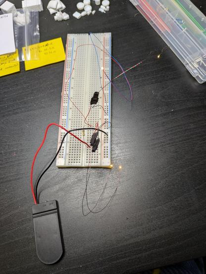 4 LEDs on long skinny wires sticking out from an electronic breadboard, with a battery pack on it. The LEDs are all on.