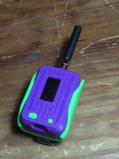 The same pager-like device in a neon green holster. A belt clip is just barely visible under the holster, which is lying on its back.