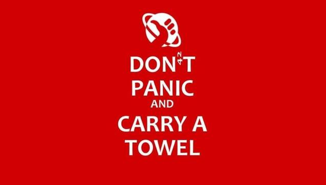 A meme using the format of Keep Calm and Carry On but the crown has been replaced with an icon for stellar hitch-hiking and the words say, "Don't Panic and Carry a Towel". There is a small 42 hidden in the image posing as an apostrophe..