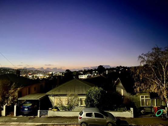 A view of the fading light. Gold melting into deep indigo y. J the foreground is a house lit with street light. There used to be also a footpath, a car and a tree.