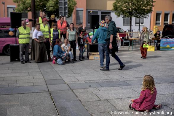 personen des gegenprotest sammeln sich für ein kleines gruppenbild, davor ein kleines kind, das mit kreide herzen auf den boden malt