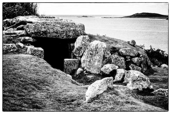 The entrance to a bronze age burial chamber with large stones and a capstone above. In the background is the sea and an island near the horizon.