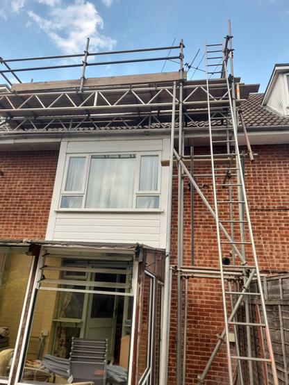 the back of a red brick townhouse with a conservatory, with scaffolding around it up to the roof.