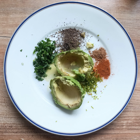 Die genannten Zutaten auf einem Teller. Die Avocado ist halbiert und der Kern und die Schale entfernt.