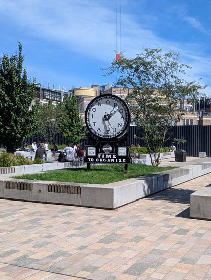 Large clock standing in the middle of a university square. Instead of numbers, it has the word 'organization'