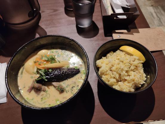 A photo of a meal. You see two bowls, one filled with off-yellow soup, vegetables, and meat. The other has spiced rice and a lemon wedge.