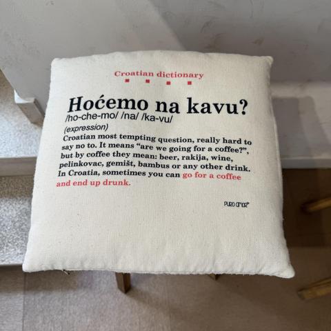 A square cushion on a stool in a cafe, with the below text:

Croatian dictionary

Hocemo na kavu?
/ho-che-mo/ /na/ /ka-vu/ (expression)

Croatian most tempting question, really hard to say no to. It means "are we going for a coffee?" but by coffee they mean: beer, rakija, wine, pelinkovac, gemist, bambus or any other drink. In Croatia, sometimes you can go for a coffee and end up drunk.