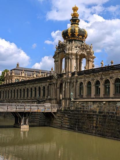 Blick über eine Brücke die über Wasser führt auf Schloss Mauer. Leicht bewölkter Himmel.