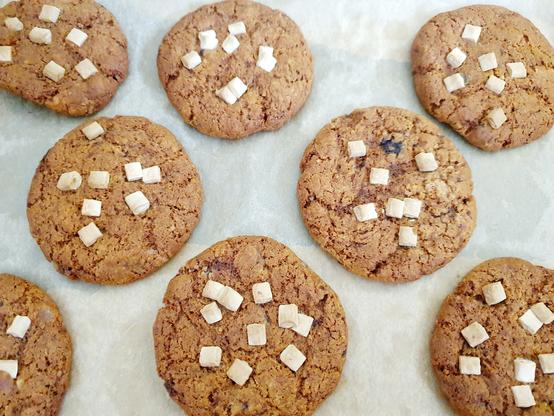 8 ginger biscuits can be seen on baking paper. They are the golden brown of ginger, with a smattering of white chocolate chips on each one. They are very hot and will be transferred to a baking rack soon. The next batch of 8 are in the oven.