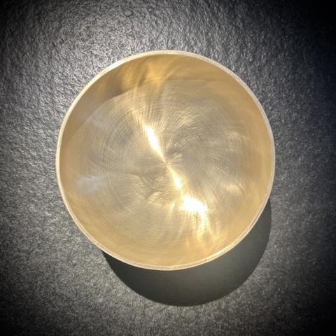 Runde Klangschale aus Messing vor dunklen Steinhintergrund fotografiert.