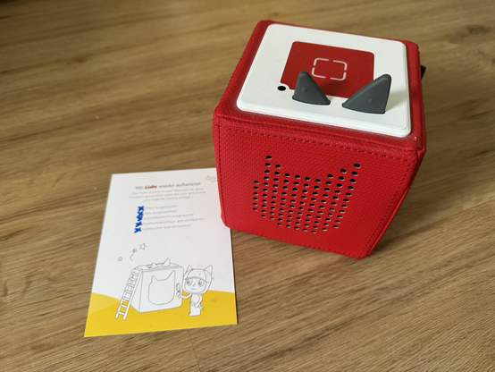 Eine rote Toniebox mit einem Zettel der Werkstatt, auf dem die Wartung abgezeichnet ist.