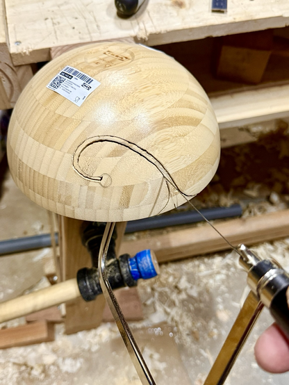 Bowl held upside down in the vice, with the curl shape traced out and mostly cut with the coping saw still in the kerf.