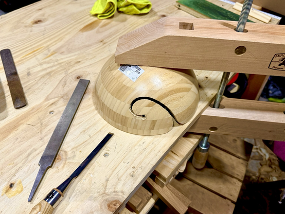 The bowl held upside down on a workbench with a screw clamp, with a file next to it.