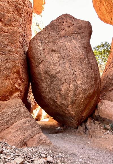 Walking trail squeezes under this large red boulder in Morocco.
