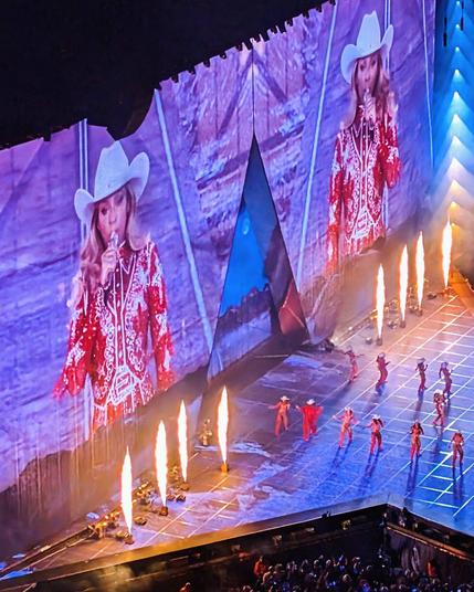 Beyoncé on stage in a sparkly red cowgirl outfit, several dances in matching red outfits and flames shooting up above the screen