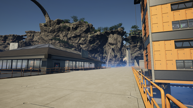 A view looking east shows the modest building housing the Circuit Board factory on the left and the orange Copper Sheet factory on the right. Waterfalls can be seen flowing from the cliff tops in the background.