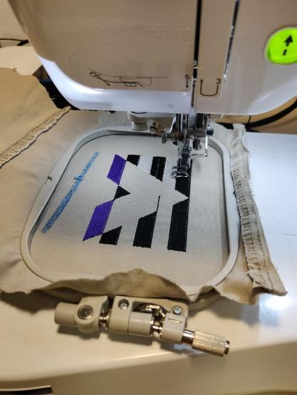 Stickmaschine zum Beginn eines Stickvorgangs für eine Straight Ally Pride Flag, die schwarzen Streifen und der lila Teil sind bereits gestickt