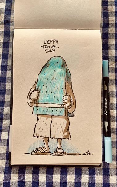 Arthur Dent is holding a large light blue towel, covering his head. The character is dressed in a bathrobe and sandals. Above, the text reads "HAPPY TOWEL DAY."