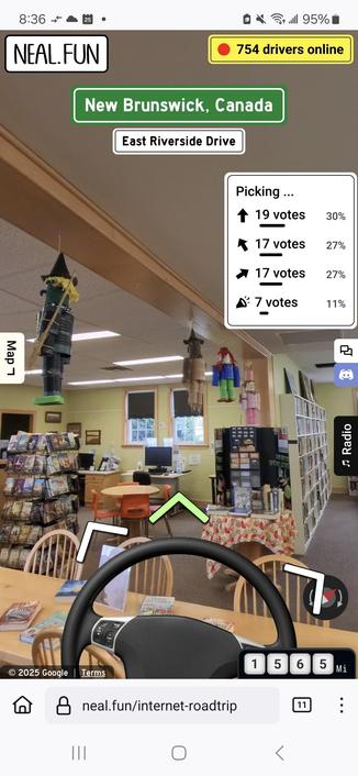 interior of a library with yellow walls, shelves of books, tables & chairs, & various doll figures hanging from the ceiling beams.  a car steering wheel is superimposed over top.