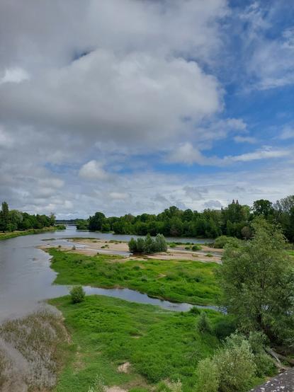 Ciel bas nuageux et ciel bleu en arrière, îles de Loire sableuses et reverdies ,le fleuve en méandres et des arbres dans le lointain. Encore plus en arrière  le pont de fil