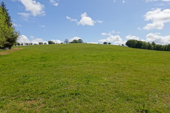 A large grassy hill fills the foreground of the image, above which is a blue sky with white clouds. It is vaguely reminiscent of the classic Windows 95 desktop image.