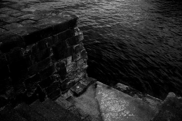 Dark stones made of volcanic rocks are made into a wharf, steps lead down to the dark water, an iron ring rusts on a step