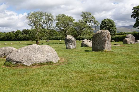 A variety of large standing stones (although some have fallen) in a field. In the middle distance more stones can be seen on the opposite side of the circle.