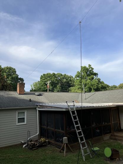 The back yard of a house, with a wire dipole antenna suspended from a the roof's exhaust chimney and a coaxial cable dropping to the ground.