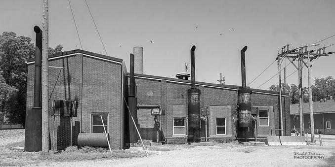 Exterior view of a very small municipal electric power plan with four exhaust stacks outside the brick building.