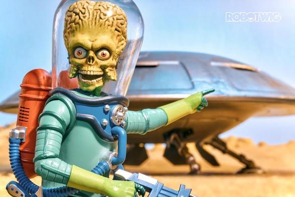 Mars Attacks Alien points over at UFO in desert landscape
