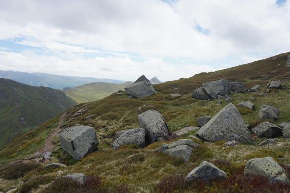 Une prairie d'altitude avec de gros rochers épars. L'un d'entre eux a la même forme qu'un relief situé à l'arrière-plan.