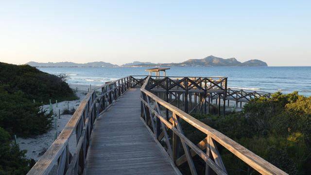 A photo of a raised boardwalk leading to the shore of a bay. There are hills on the far shore. The sky is clear and the sun light is fading.