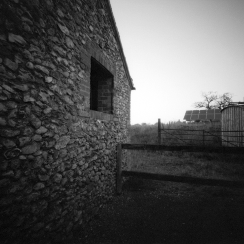Photograph looking along the side of a barn, with an array of solar panels in the background