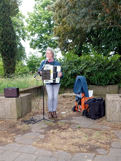 Eine Musikerin singt zum Akkordeon, imHintergrund Bäume und Büsche