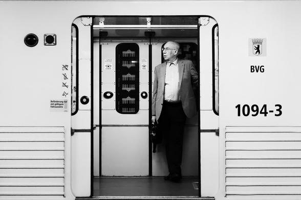 black and white. landscape format. street scene in the berlin subway. An elderly dapper gentleman stands in the entrance area of a subway with the door open, as if staged.