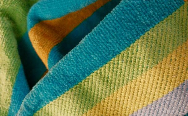 Close-up photo of a towel with colorful stripes in blue, green, gold, and silver.